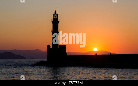 Die silhoutte der Leuchtturm im Hafen von Chania, eine Stadt auf der Insel Kreta, Griechenland bei Sonnenuntergang mit Menschen sitzen auf der Hafenmauer. Stockfoto