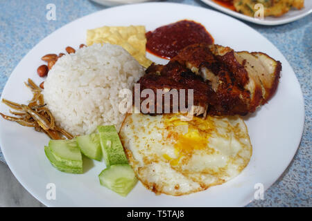 Nasi Lemak, Malaysische coconut Rice mit Spiegelei, Gurken serviert, frittierte Sardellen, Erdnüssen und Fried Chicken in Chili Sauce gekocht Stockfoto