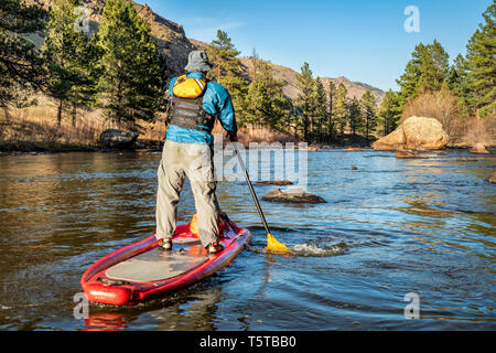 Ältere männliche Paddeln aufblasbare Stand up paddleboard auf einem Berg River - Poudre RIver in den Colorado im Frühjahr Landschaft mit geringer Wasserströmung Stockfoto