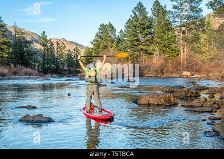 Ältere männliche Paddeln aufblasbare Stand up paddleboard auf einem Berg River - Poudre RIver in den Colorado im Frühjahr Landschaft mit geringer Wasserströmung Stockfoto