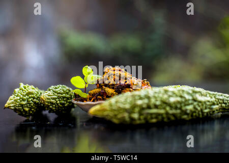 Beliebtes Gericht für das Mittagessen serviert d.h. bitteren Kürbis mit Gewürzen und Gemüse auf Holz- Oberfläche in eine Glasplatte mit rohen Karela, Nähe zu sehen. Stockfoto