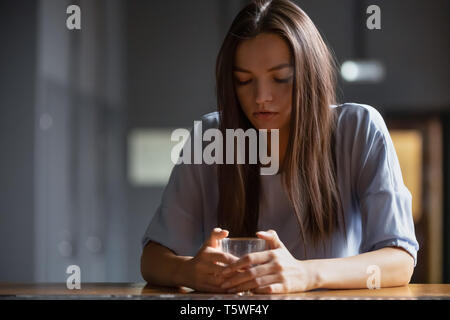 Nachdenkliche junge Frau sitzt auf der Theke trinken Alkohol Stockfoto