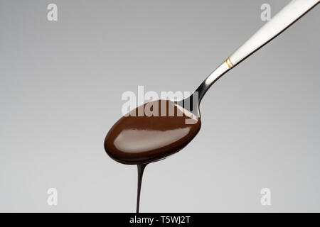 Flüssige Schokolade auf einem Löffel auf Hellgrau backgiund Stockfoto