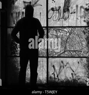 Mann durch Das zerbrochene Fenster eines verlassenen Gebäude suchen. Schwarz und Weiß. Stockfoto