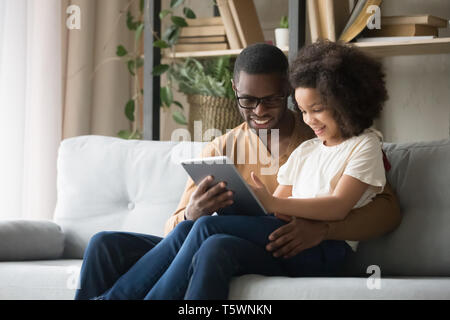 Afrikanischen Vater hält auf dem Schoß Tochter Spaß mit Tablet Stockfoto