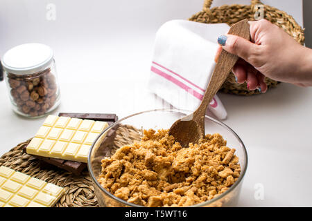 Eine Frau, die 3 Schokoladen Kuchen Torte Zutaten auf den Tisch. Küche mit weisser, dunkler und Milchschokolade. Haselnüsse jar. Kekse Teig Stockfoto