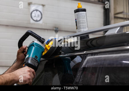 Nahaufnahme auf die Hände eines Mannes, der Arbeiter, der hält ein Werkzeug Polierer zum Polieren das Dach eines Autos während der Arbeit in einem Fahrzeug mit Werkstatt. Au Stockfoto