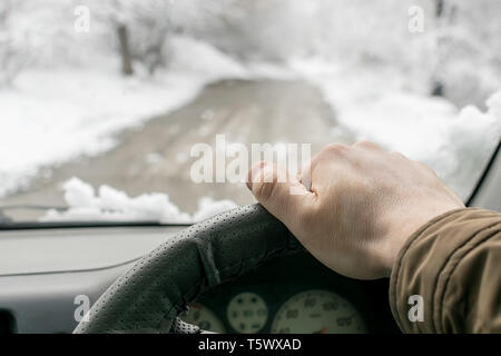 Des Menschen Hand am Lenkrad eines Autos, die in den verschneiten Wald auf einem nassen matschigen Weg bewegt Stockfoto