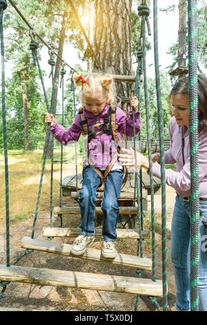 Mutter hilft, seine kleine Tochter Hindernisse in Abenteuer Klettern High Wire Park, aktiven Lebensstil der Kinder. Stockfoto