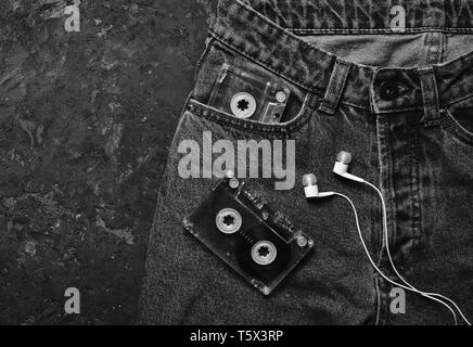 Jeans, Hörkassette, Kopfhörer Layout auf schwarzem Beton Tabelle. Konzeptionelle Foto illustriert die Faszination der Musik zu hören. Ansicht von oben. Stockfoto