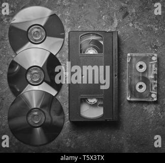 Flach Videokassetten, CDS, audio Kassette auf einem schwarzen Betonoberfläche. Retro media Technologie der Vergangenheit an. Ansicht von oben. Stockfoto