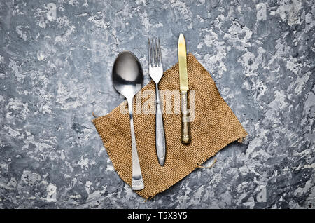 Antike Löffel, Gabel, Messer auf eine Serviette liegen auf einem grauen Beton Tabelle. Ansicht von oben. Stockfoto