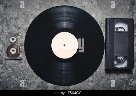 Schallplatte, Audio- und Videokassetten auf einem grauen Betonflächen. Retro media Technologie aus den 80er Jahren. Ansicht von oben. Stockfoto