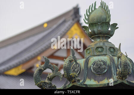 Im Vordergrund eine detaillierte japanische Giessen/Skulptur mit Fisch eingerichtet, im Hintergrund einen japanischen Tempel mit goldenen Highlights Stockfoto