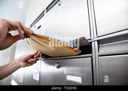 Nahaufnahme der Hand Einfügen einer Person Umschläge in der Mailbox Stockfoto