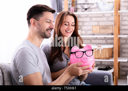 Lächelnde junge Paar sitzt auf einem Sofa Holding rosa Sparschwein Stockfoto