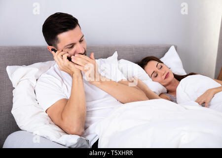 Junge Mann auf dem Smartphone Neben seiner Frau schlafend auf dem Bett im Schlafzimmer Stockfoto