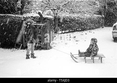 Zwei Jungen entlang der unteren Straße, Medstead Lymington, Hampshire, England, Vereinigtes Königreich rodeln. Stockfoto