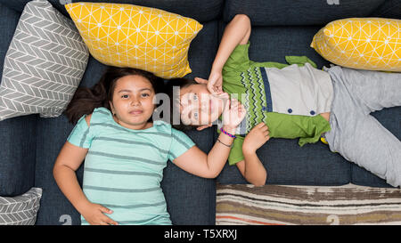 Asien/kaukasischen Bruder und Schwester auf einem Sofa zusammen lächelnd direkt in die Kamera schauen, Gemischt.