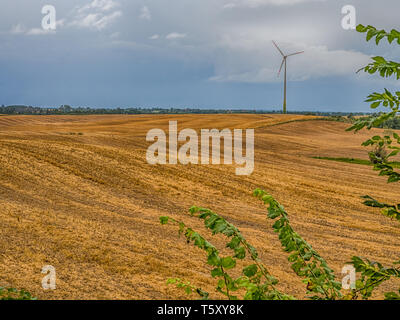 Den Furchen des Feldes auf den Hügeln mit einer Windkraftanlage. Es ist ein Gerät, dass die kinetische Energie des Windes in elektrische Energie umwandelt. Polen. Osten Stockfoto