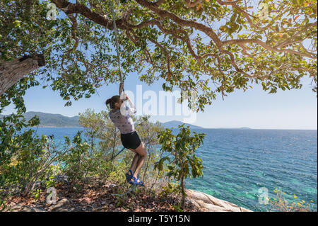 Junge Frau hängenden Seil mit Baum im tropischen Meer auf der Insel Stockfoto