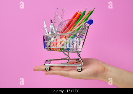 Shopping Cart mit Mitarbeitern der Schule halten in der hand Bleistifte Herrscher Kompass Stockfoto