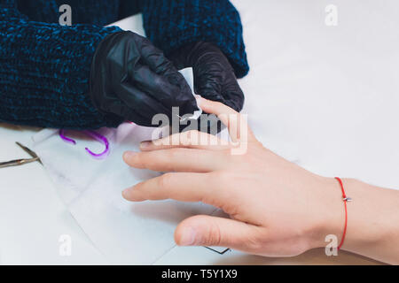 Hände in Handschuhen kümmert sich um Hand Nägel Mann. Maniküre Beauty Salon. Stockfoto