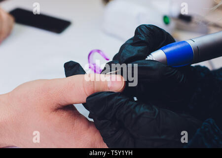 Hände in Handschuhen kümmert sich um Hand Nägel Mann. Maniküre Beauty Salon. Stockfoto