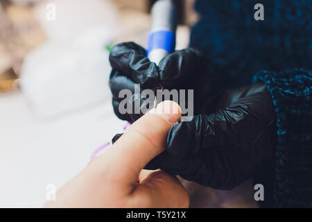 Hände in Handschuhen kümmert sich um Hand Nägel Mann. Maniküre Beauty Salon. Stockfoto