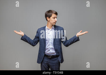 Portrait von stattlicher Junge lächelnde Mann in Anzug, die Wahl zwischen zwei Produkten auf seine Handflächen zu machen Stockfoto