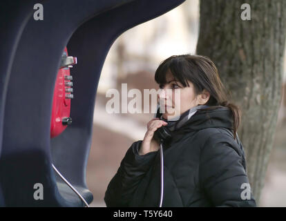 Attraktive junge Frau, die von einem roten Straße Telefonzelle. Stockfoto