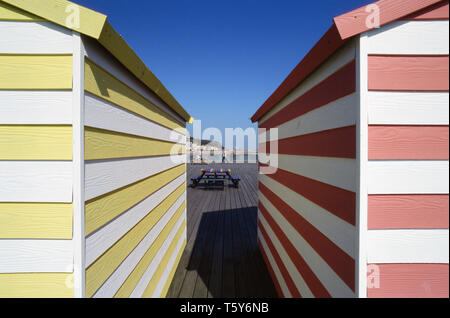 Bunten Badekabinen am Pier von Hastings, East Sussex, UK, mit Passanten und Hastings direkt am Meer in der Ferne Stockfoto
