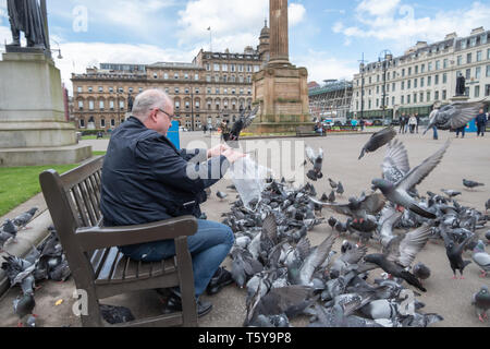 Glasgow, Schottland, Großbritannien. 27.April 2019. UK Wetter. Ein Mann sitzt auf einer Bank, die Fütterung der Tauben auf einem sonnigen Nachmittag auf dem George Square. Credit: Skully/Alamy leben Nachrichten Stockfoto