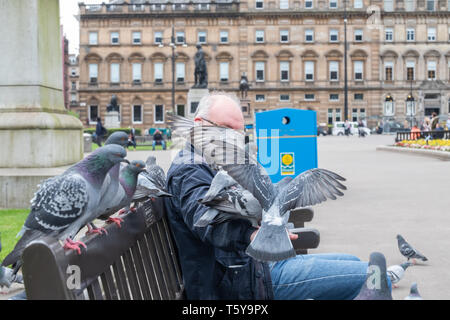 Glasgow, Schottland, Großbritannien. 27.April 2019. UK Wetter. Ein Mann sitzt auf einer Bank, die Fütterung der Tauben auf einem sonnigen Nachmittag auf dem George Square. Credit: Skully/Alamy leben Nachrichten Stockfoto