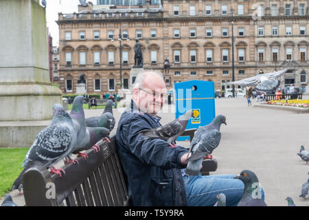 Glasgow, Schottland, Großbritannien. 27.April 2019. UK Wetter. Ein Mann sitzt auf einer Bank, die Fütterung der Tauben auf einem sonnigen Nachmittag auf dem George Square. Credit: Skully/Alamy leben Nachrichten Stockfoto