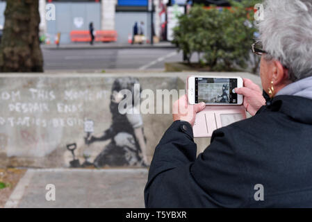 London, Großbritannien. 27. April 2019. Eine Frau, die Aussicht auf ein Kunstwerk, das an einer Wand im Marble Arch nach zehn Tagen der Proteste in London vom Aussterben Rebellion, eine Gruppe fordert, dass Regierungen Maßnahmen zur Bekämpfung des Klimawandels erschienen ist. Jetzt in einer Schutzhülle aus Kunststoff abgedeckt, das Kunstwerk ist der gefeierte Street Artist Banksy zugeschrieben worden und stellt ein Bild von einer Pflanze und ein Mädchen, dass eine Gartengeräte mit dem Aussterben Rebellion Logo neben dem Text "Von diesem Moment der Verzweiflung enden und Taktik beginnen". Credit: Stephen Chung/Alamy leben Nachrichten Stockfoto