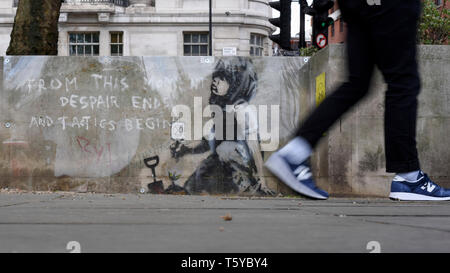 London, Großbritannien. 27. April 2019. Ein Mann durch ein Kunstwerk, das an einer Wand im Marble Arch nach zehn Tagen der Proteste in London vom Aussterben Rebellion, eine Gruppe fordert, dass Regierungen Maßnahmen zur Bekämpfung des Klimawandels erschienen ist. Jetzt in einer Schutzhülle aus Kunststoff abgedeckt, das Kunstwerk ist der gefeierte Street Artist Banksy zugeschrieben worden und stellt ein Bild von einer Pflanze und ein Mädchen, dass eine Gartengeräte mit dem Aussterben Rebellion Logo neben dem Text "Von diesem Moment der Verzweiflung enden und Taktik beginnen". Credit: Stephen Chung/Alamy leben Nachrichten Stockfoto