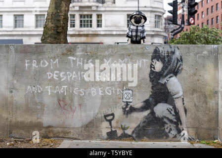 London, Großbritannien. 27. April 2019. Lilie der Mops sitzt neben einem Kunstwerk, das an einer Wand im Marble Arch nach zehn Tagen der Proteste in London vom Aussterben Rebellion, eine Gruppe fordert, dass Regierungen Maßnahmen zur Bekämpfung des Klimawandels erschienen ist. Jetzt in einer Schutzhülle aus Kunststoff abgedeckt, das Kunstwerk ist der gefeierte Street Artist Banksy zugeschrieben worden und stellt ein Bild von einer Pflanze und ein Mädchen, dass eine Gartengeräte mit dem Aussterben Rebellion Logo neben dem Text "Von diesem Moment der Verzweiflung enden und Taktik beginnen". Credit: Stephen Chung/Alamy leben Nachrichten Stockfoto