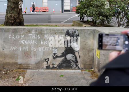 London, Großbritannien. 27. April 2019. Eine Person, die Aussicht auf ein Kunstwerk, das an einer Wand im Marble Arch nach zehn Tagen der Proteste in London vom Aussterben Rebellion, eine Gruppe fordert, dass Regierungen Maßnahmen zur Bekämpfung des Klimawandels erschienen ist. Jetzt in einer Schutzhülle aus Kunststoff abgedeckt, das Kunstwerk ist der gefeierte Street Artist Banksy zugeschrieben worden und stellt ein Bild von einer Pflanze und ein Mädchen, dass eine Gartengeräte mit dem Aussterben Rebellion Logo neben dem Text "Von diesem Moment der Verzweiflung enden und Taktik beginnen". Credit: Stephen Chung/Alamy leben Nachrichten Stockfoto