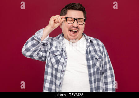 Portrait von Angeregten lustig aussehenden Mann im mittleren Alter business casual kariertem Hemd und Brille ständigen Holding seine Brille und mit einem Augenzwinkern. Stockfoto