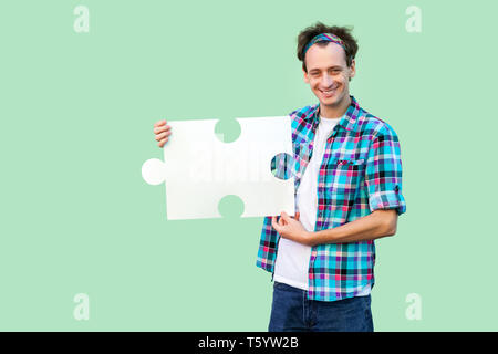 Gerne hübscher junger Mann in kariertem Hemd und mit großen Stück des Puzzles, an Kamera suchen mit toothy Lächeln. Hallenbad, isoliert, Kopie sp Stockfoto