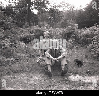 1940, historische, eine elegant gekleidete Herr und Dame auf dem Gras von einem Pfad in Ruislip Woods, West London, England, UK. Das Holz - jetzt ein Naturschutzgebiet - ist der größte Block der alten naturnahen Wald im Großraum London. Stockfoto