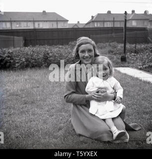 1940, historische, in einem Garten, Vororte, Ruislip, West London, ein lächelndes Mädchen kniend auf dem graass Holding in ihren Armen ihre kleine Schwester. Stockfoto