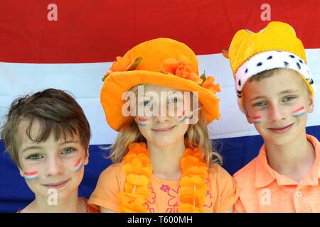 Drei niederländische Kinder gekleidet in Orange vor der Flagge der Niederlande Stockfoto