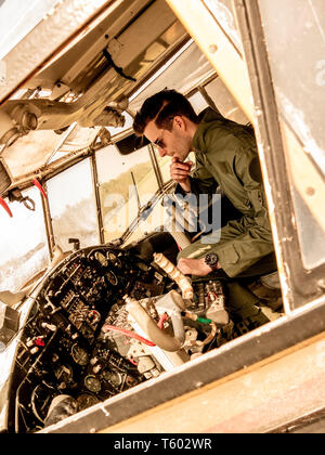Ein hübscher junger Mann Pilot in einem grünen insgesamt im Cockpit eines alten Platanen an einem sonnigen Tag sitzen. Stockfoto