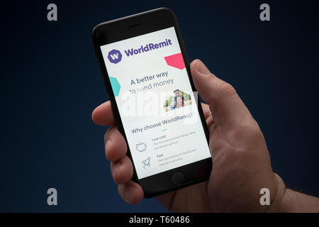 Ein Mann schaut auf seinem iPhone die zeigt die WorldRemit Logo (nur redaktionelle Nutzung). Stockfoto