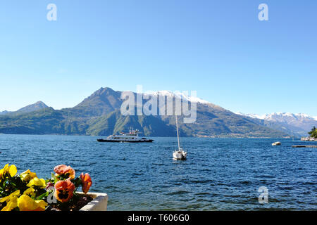 Schönen Panoramablick auf den Comer See von Varenna am Seeufer, ein Passagierschiff verschieben und Berge mit Schnee im Hintergrund, im sonnigen Tag abgedeckt. Stockfoto