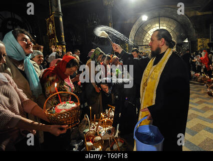 Ein orthodoxer Priester gesehen Segen die traditionelle Ostern Kuchen und bemalte Eier für das Osterfest im Pechersk Lavra Kirche Christlich-orthodoxen Gläubigen bereit Ostern mit einem heiligen Feuer Zeremonie, die die Auferstehung Christi feiern. Stockfoto