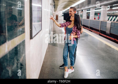 Junger Mann und Frau mit der U-Bahn. Paar in der U-Bahn. Stehend an der Wand und zeigen. Fröhliches Lächeln. In Valentine's Tag. Leger kleiden Stockfoto