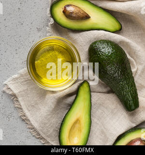 Hälften und ganze Avocados und Schüssel von Öl auf Serviette Stockfoto